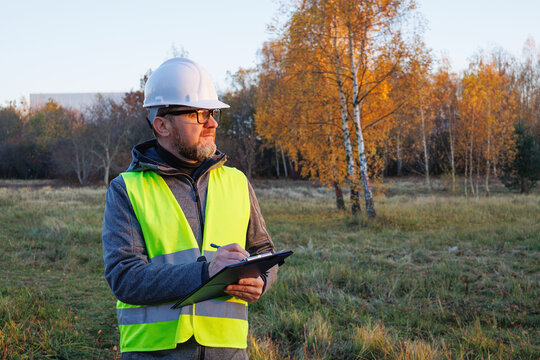 Matured male professional working on a vacant field, a new construction site. Environmental engineer or land surveyor conducting site inspection and territory analysis.