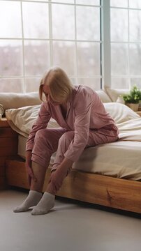 Senior woman rubbing swollen legs while sitting on bed, varicose veins pain
