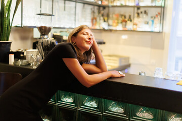 Woman leans on bar counter in a lively setting during the evening hours