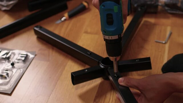 Metal chair fixed on wooden surface. Installing chair base with cordless tool and hardware. Securely attaching metal chair base to wooden floor using power drill