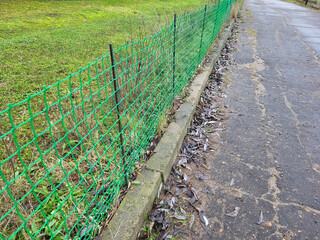 A green plastic mesh fence on a grassy lawn near the road