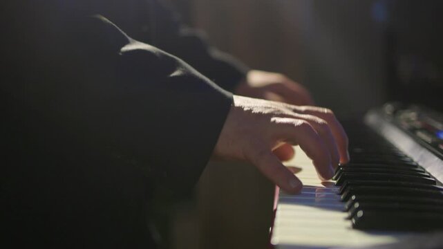 Hands craft ambience. Musician creates mellow synth sounds. Fingers manipulate keyboard under atmospheric lighting. Closeup of musician blending sounds under dim stage illumination