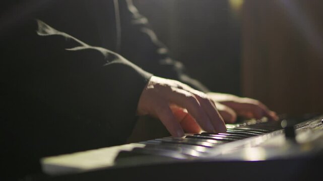 Hands craft ambience. Musician creates mellow synth sounds. Fingers manipulate keyboard under atmospheric lighting. Closeup of musician blending sounds under dim stage illumination