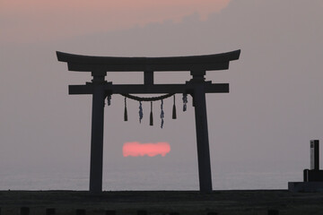 鳥居と雲の切れ間から昇る太陽