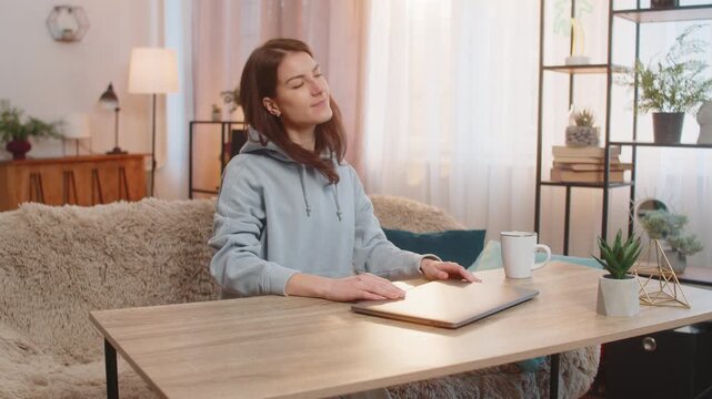 Young woman freelancer closing laptop stretches back and looks joyfully finalizing the successful end of workday and readiness to relax. Caucasian girl relaxing taking a break up sitting at table