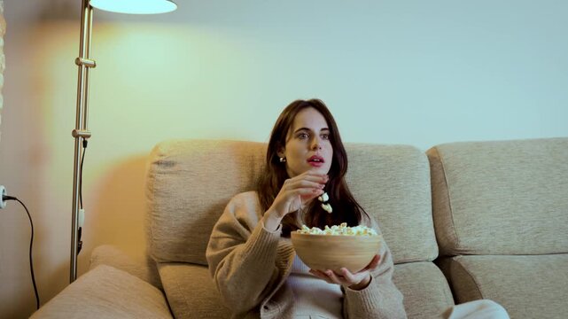 Young woman eating popcorn watching a movie at home