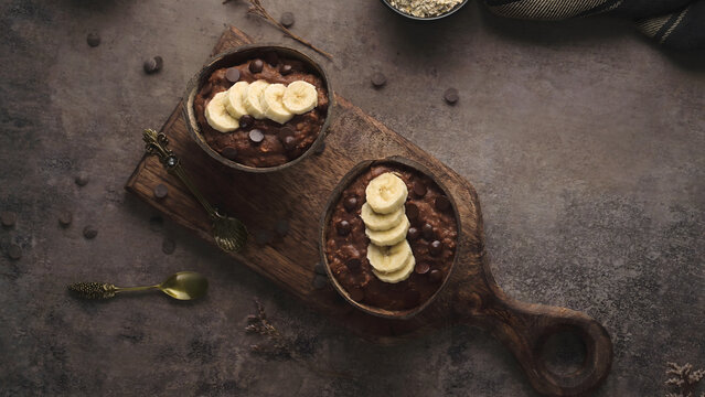 Chocolate Banana Protein Oatmeal in Coconut Bowls on a Rustic Wooden Board