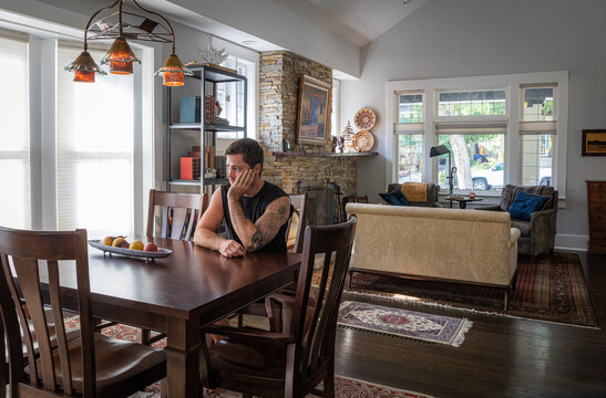 Young strong athletic man with tattoos at a dining room table inside a house. 