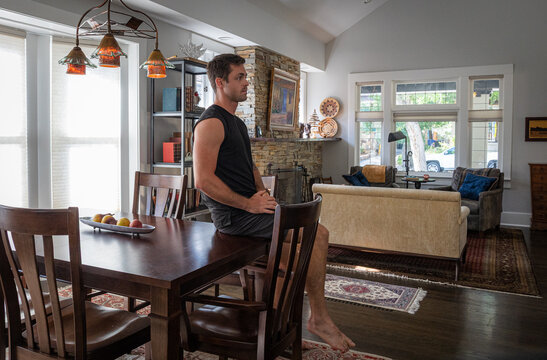 Young strong athletic man with tattoos at a dining room table inside a house. 