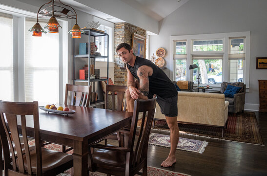 Young strong athletic man with tattoos at a dining room table inside a house. 