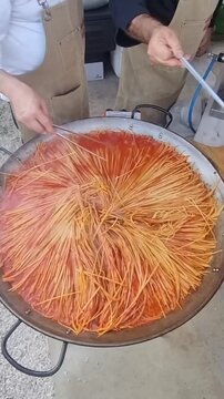 preparazione degli spaghetti all'assassina in un pentolone durante un evento all'aperto