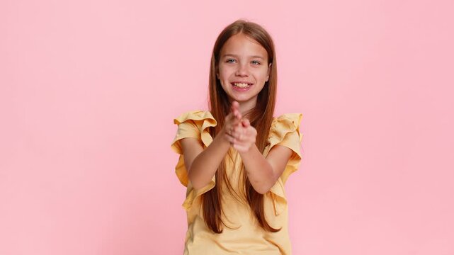 Young child girl enthusiastically mimics a finger gun gesture smiling with excitement and looking directly into the camera pretending to shoot in a playful humorous way. School kid on pink background