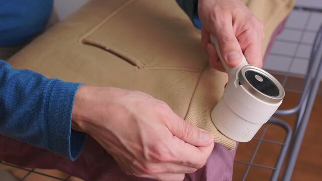 User carefully experiences lint removal on clothing in laundry space. Practical tutorial showcasing how to refresh garments using electric lint shaver in cozy setting