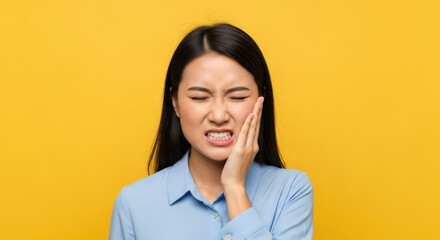 Fototapeta premium Young adult experiencing significant facial discomfort while clutching cheek against bright background