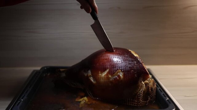 Roasted pork knuckle on baking tray as large knife starts slicing meat close up scene of festive dinner preparation at home kitchen with hearty food and warm holiday atmosphere