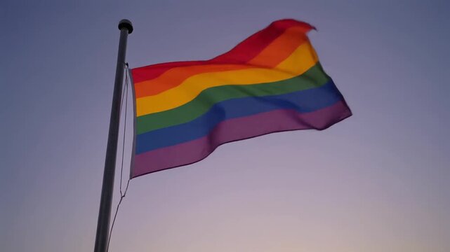 Vibrant rainbow flag proudly waving against a gradient twilight sky, symbolizing diversity, equality, and the global movement for acceptance and love