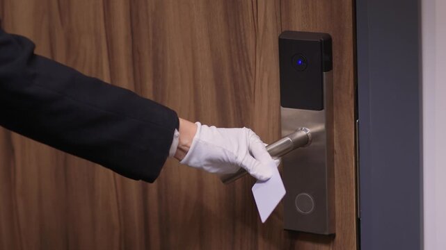 Guest room keycard insertion. Professional service in quiet luxurious hotel corridor. Formal suit sleeve suggesting concierge unlocking guest room door in subdued lighting