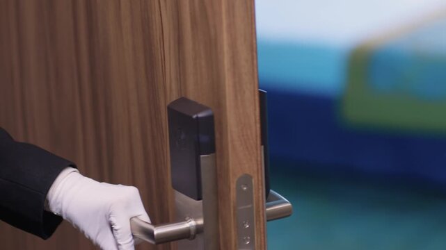 Guest room keycard insertion. Professional service in quiet luxurious hotel corridor. Formal suit sleeve suggesting concierge unlocking guest room door in subdued lighting