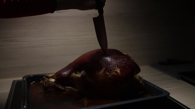 Close up of baked meat on oven tray hand piercing roast with large knife juicy interior and meat juice flowing slow motion cooking scene