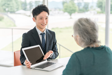 Obraz premium A businessman who consults with a senior woman and makes suggestions using a laptop (asset management, insurance, finance)