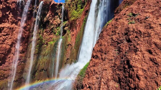 Scenic view of Ouzoud Falls in Morocco, North Africa, with a vibrant rainbow forming over powerful cascading water. Natural landscape showcasing mist, flowing water, and dram