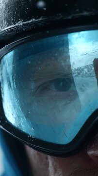 Close-up of a skier's eye reflected in blue goggles against a snowy mountain landscape