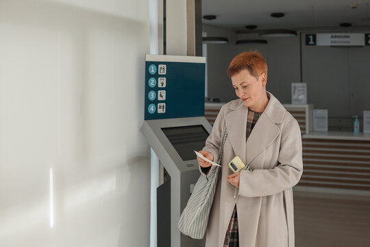 Middle aged woman taking queue ticket at reception desk in public service center, waiting for appointment