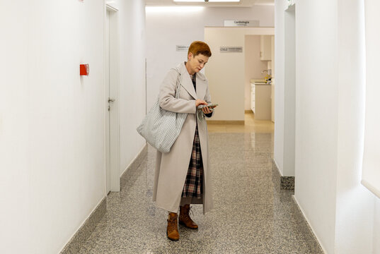 Middle aged woman taking queue ticket at reception desk in public service center, waiting for appointment