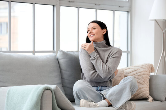 Beautiful young woman hugging herself on sofa at home