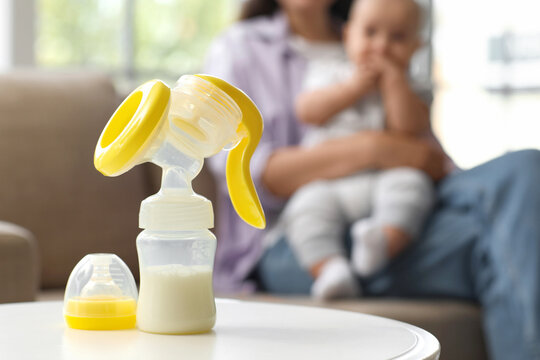 Breast pump on table against mother with baby at home, closeup