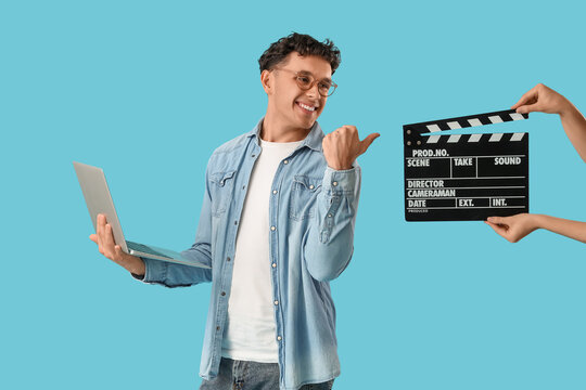 Male screenwriter with laptop pointing at female hands and movie clapper on blue background