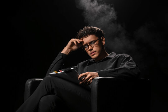 Male screenwriter with scenario in armchair on dark background