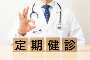 「定期健診」と書かれたブロックとOKサインをする医師