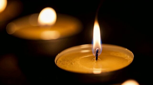 Macro shot of tea light candle flame with blurred background lights. Romantic and peaceful candlelight for celebration, anniversary, or memorial remembrance. Warm aesthetic lighting.