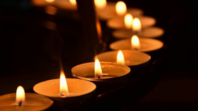 Row of Glowing Tea Light Candles in a Curved Pattern for Religious Ceremony, Remembrance, Hope, and Relaxation. Warm Candlelight Flame on Dark Surface for Funeral or Meditation Backdrop.