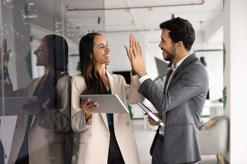 Happy successful teammates exchanging high five stands next to blackboard with written records,...