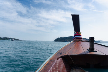 A nautical speed boat and luxury yacht cruise past the coastal lighthouse toward a summer island harbor, where the blue ocean water meets the cloudy sky