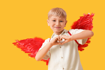 Obraz premium Cute little happy boy dressed as cupid showing heart gesture on yellow background. Valentine's Day celebration