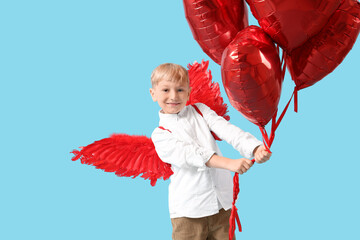 Obraz premium Cute little happy boy dressed as cupid with heart-shaped balloons on blue background. Valentine's Day celebration