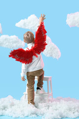 Obraz premium Cute little boy dressed as cupid in clouds on blue background, back view. Valentine's Day celebration