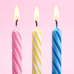 Three lit, spiraled candles with vibrant, pink, yellow, and blue stripes against a soft pink background