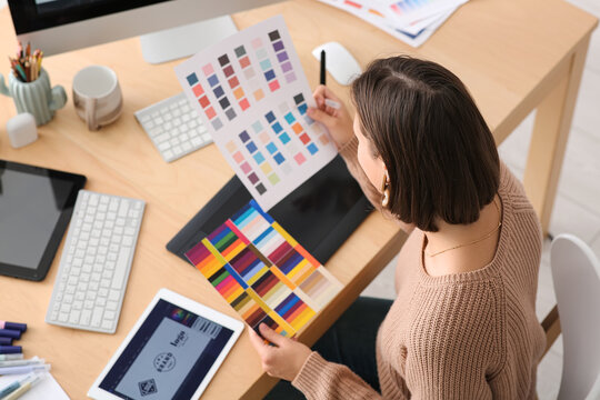 Young female graphic designer working with color samples at table in office