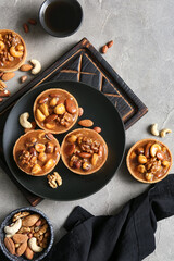 Fototapeta premium Tasty tarts with nuts and caramel sauce on plate against grunge grey background