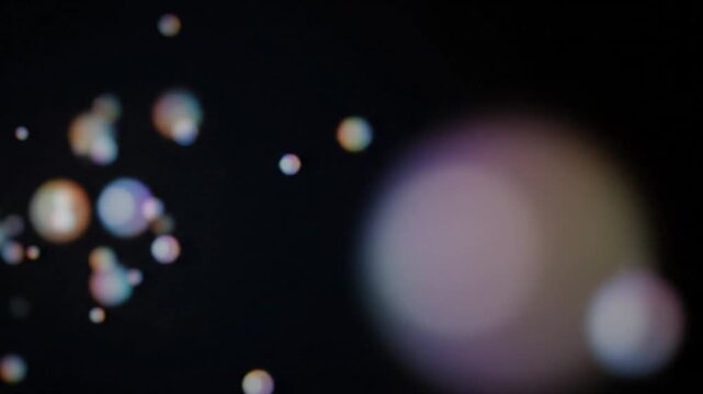 Abstract background features a dynamic scattering of colorful bokeh light orbs against a deep black void symbolizing mystical energy or digital data flow in a dark environment.