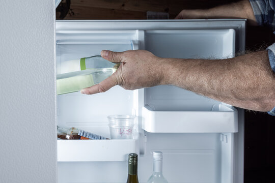 A detailed, action-oriented shot of a man's hand reaching into a brightly lit refrigerator to grab a cold bottle.