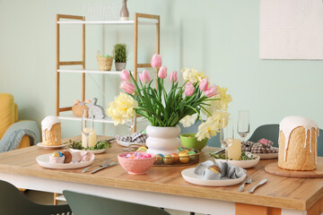 Stylish Easter table setting, painted eggs, cake and vase of flowers in dining room