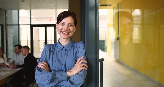 Office portrait of successful smiling businesswoman, business trainer or female coach standing in meeting room with arms-crossed, representing company management, professionalism and career growth