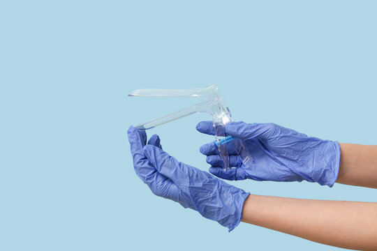 Doctor hands in medical gloves with gynecological speculum on blue background