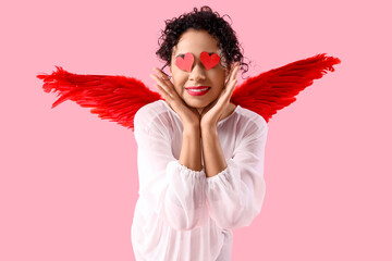 Obraz premium Young African-American woman dressed as Cupid with hearts on pink background. Valentine's Day celebration