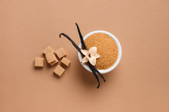 Bowl with aromatic vanilla sugar, flower and sticks on brown background
